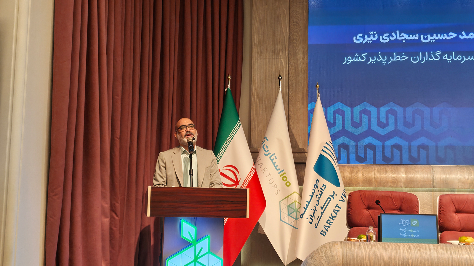 تصویر نزدیک از تندیس و نشان رویداد ۱۰۰ استارتآپ در کنار فضای برگزاری رویداد